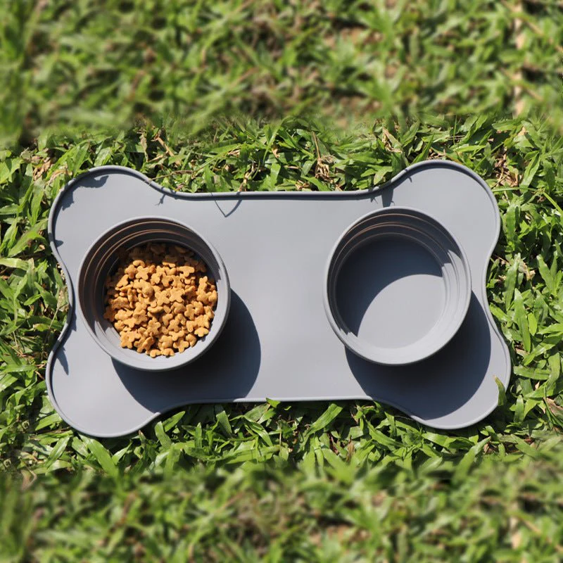Grey silicone double pet bowl on bone-shaped mat placed on grass outdoors